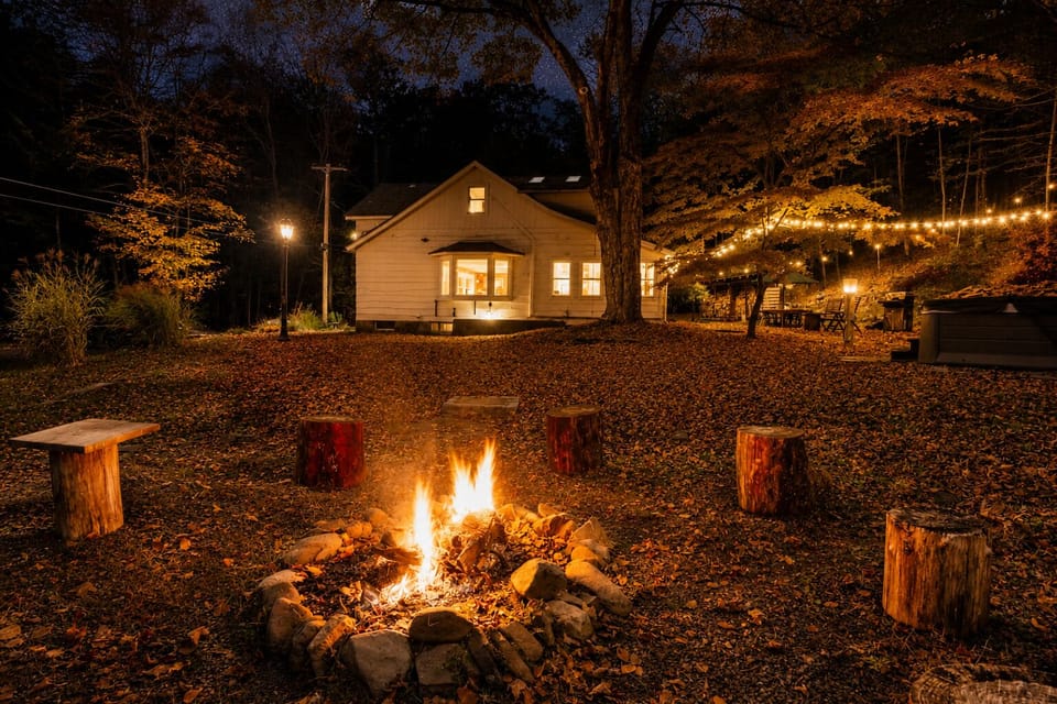 Flickering embers from the stone fire pit illuminate the backyard as autumn leaves blanket the ground. Gather around the tree stump seats for a quiet night under the string lights in this restorative, wooded Cuddebackville setting.