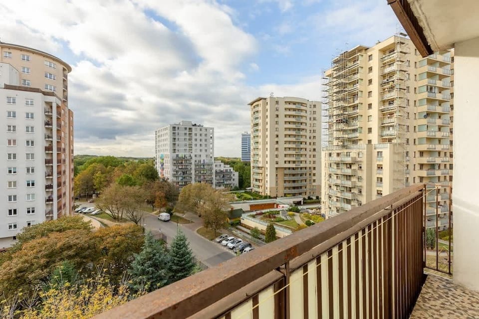 A balcony view overlooking the cityscape, surrounded by greenery and tall buildings.
