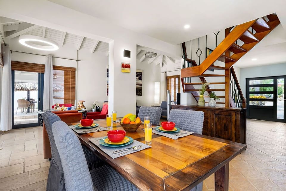 Gather around this inviting dining table, where warm wood tones and pops of color set the scene for memorable meals. Your private retreat features open-plan living with a striking staircase and airy tropical views.