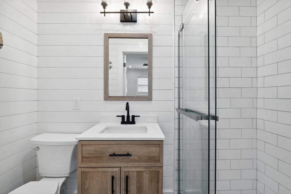 Modern bathroom featuring a wood vanity and glass-enclosed shower with white subway tile.
