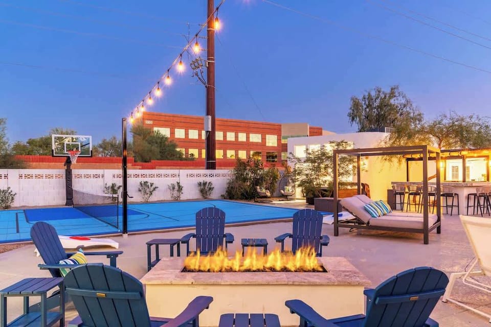 Spacious backyard featuring basketball court, fire pit with seating, shaded daybed, and outdoor bar—perfect for evening gatherings and recreation during twilight hours.
