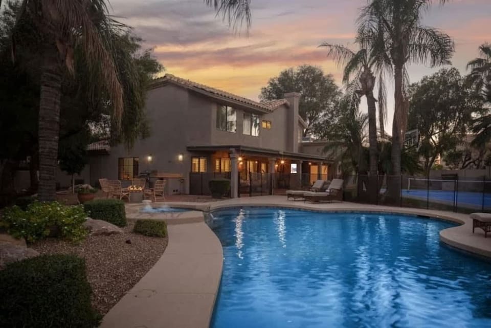 Stunning two-story vacation home with private pool set against majestic palm trees and a breathtaking sunset sky, offering an elegant desert oasis retreat.