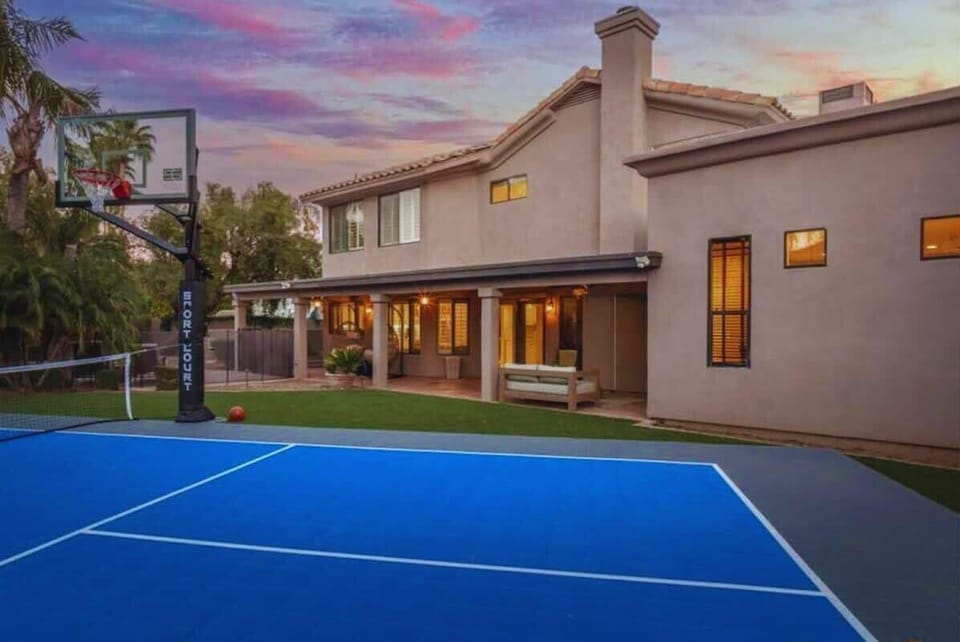 This Mediterranean-style vacation home features a private sport court and spacious outdoor areas, photographed during a colorful evening in the surrounding neighborhood.