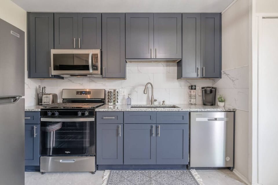 Sleek, fully updated kitchen with modern gray cabinetry, stainless steel appliances, and marble-style backsplash. Includes dishwasher, microwave, coffee station, and full-size fridge…perfect for home-cooked meals or quick bites.