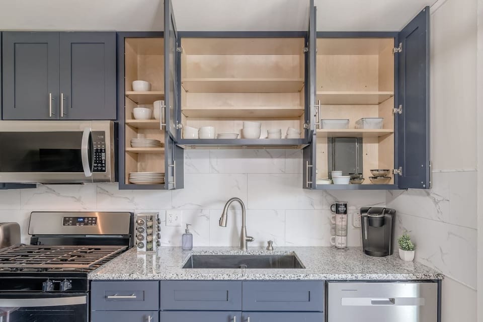 Sleek, fully updated kitchen with modern gray cabinetry, stainless steel appliances, and marble-style backsplash. Includes dishwasher, microwave, coffee station, and full-size fridge…perfect for home-cooked meals or quick bites.
