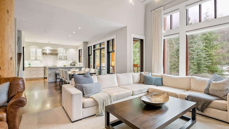- Spacious open-concept living room Whistler chalet  
- Cozy fireplace and forest views through tall windows  
- Modern design perfect for family mountain getaways  
