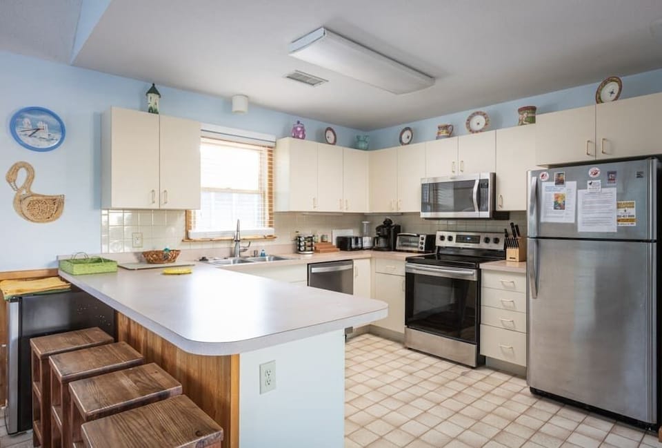 Top Level Fully Equipped Kitchen with a Refrigerator, Stove, Oven, Microwave, Dishwasher, Coffee Maker, Toaster, and Breakfast Bar Seating, Plus Natural Light from Nearby Windows