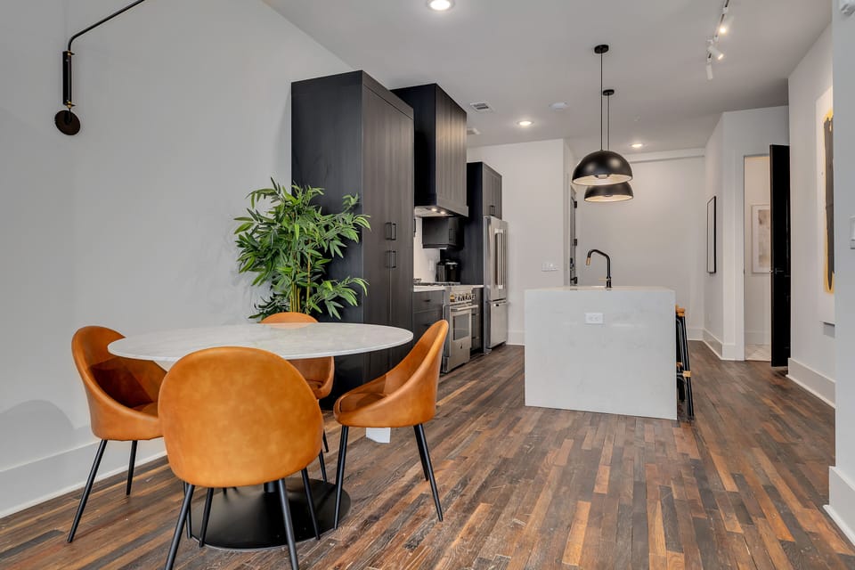 Open dining & kitchen layout w/ round table, warm wood floors & greenery