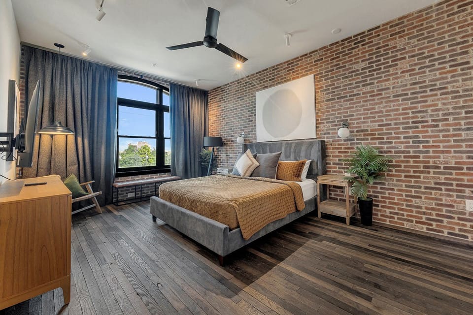 Serene bedroom w/ brick walls, large windows & layered textures for a restful retreat