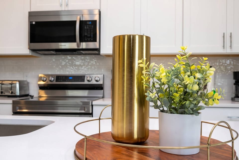 Experience a stylish kitchen that combines modern charm and practicality, featuring sleek stainless steel appliances and bright white cabinetry, complemented by a gold vase and fresh greenery for an inviting cooking space.