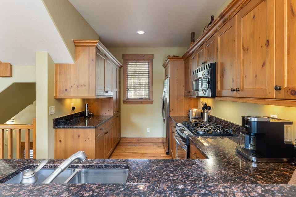A kitchen with wooden cabinets, granite countertops, stainless steel appliances, a microwave, a coffee maker, and a window with blinds.