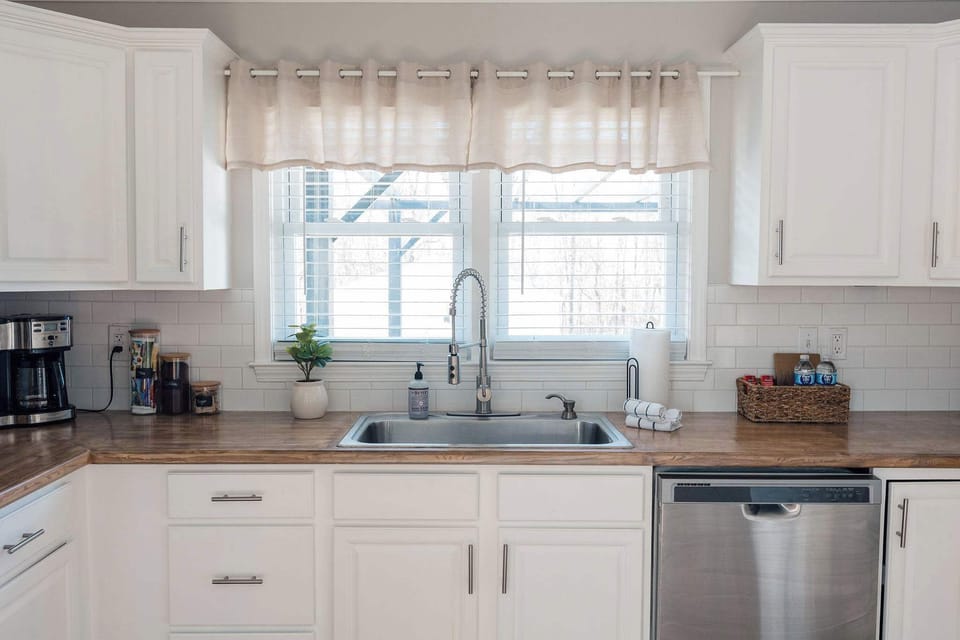 Bright, modern kitchen with stainless steel appliances, white cabinetry, and warm wood countertops. Clean, inviting space with plenty of natural light—perfect for cooking and gathering.