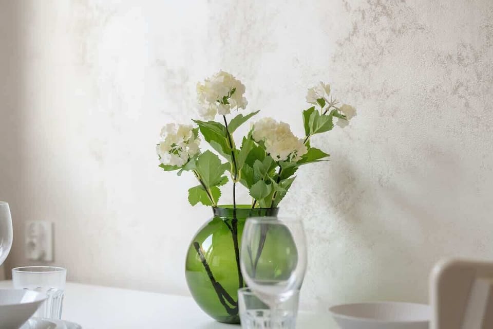 A close-up of a dining table with a green glass vase filled with fresh white flowers.






