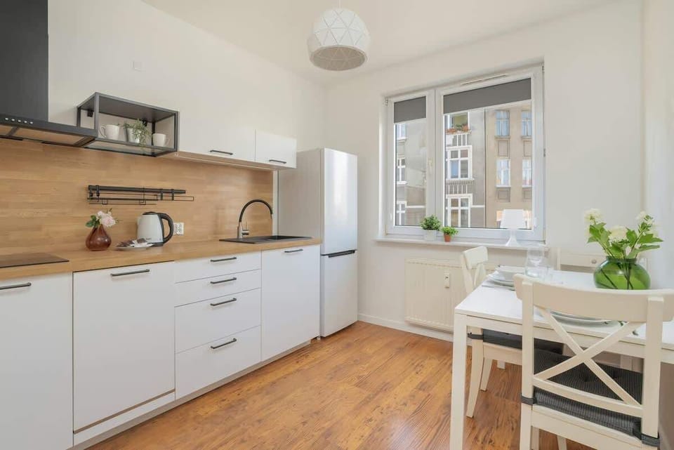 A compact kitchen with white cabinets, a wooden backsplash, and a small dining table.
