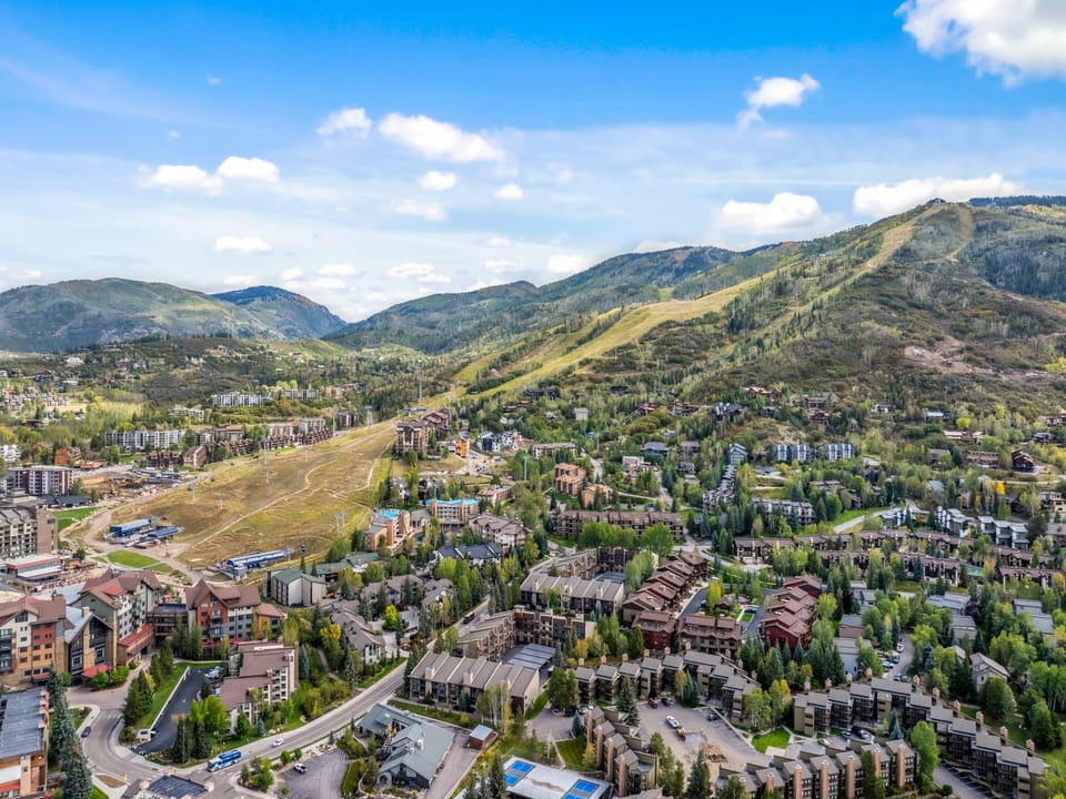 Aerial view of a mountain resort community, surrounded by forested peaks and alpine terrain, offering proximity to year-round outdoor recreation and scenic natural beauty.
