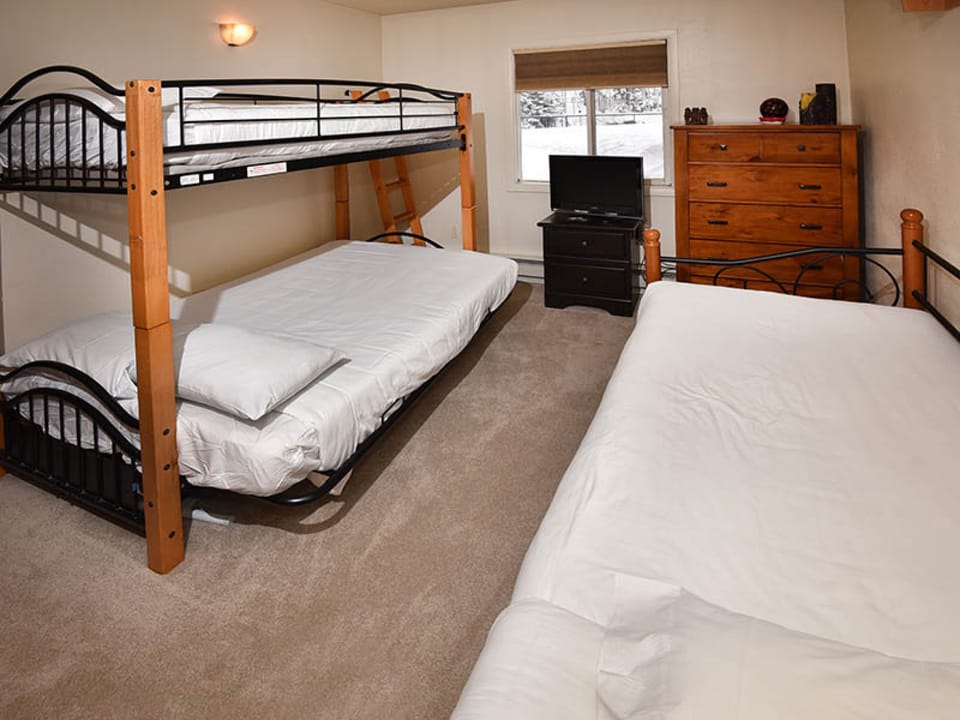 Your group-friendly bedroom sleeps everyone comfortably with a bunk bed and full bed, all dressed in crisp white linens. Natural light streams in while warm wood furniture adds a cozy, welcoming touch.