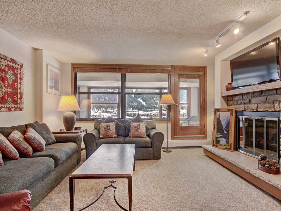 Cozy living room with TV and fireplace, access to enclosed porch.