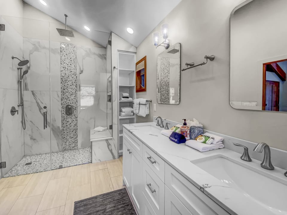 Indulge in the primary ensuite bathroom, a spa-like retreat featuring a spacious walk-in shower with a built-in bench, dual vanity sinks, and ample storage for a luxurious and comfortable stay.