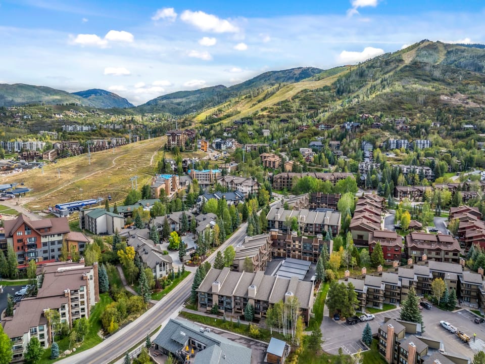 Aerial view of the resort community nestled in the valley, with ski slopes and mountain peaks in the background. This property is part of a scenic mountain village known for year-round recreation.