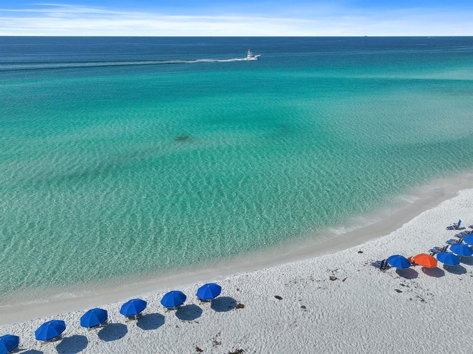 Pristine white sand beach with crystal-clear turquoise waters and colorful umbrellas dotting the shoreline.