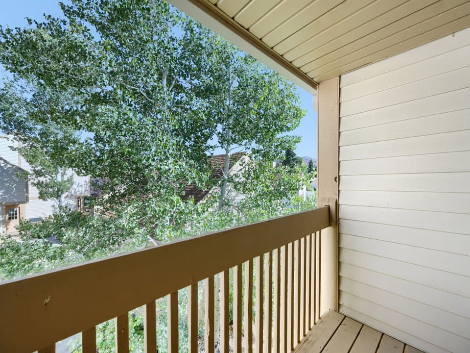 A covered balcony overlooks a peaceful neighborhood framed by leafy trees, offering a quiet spot to enjoy the surrounding residential area.