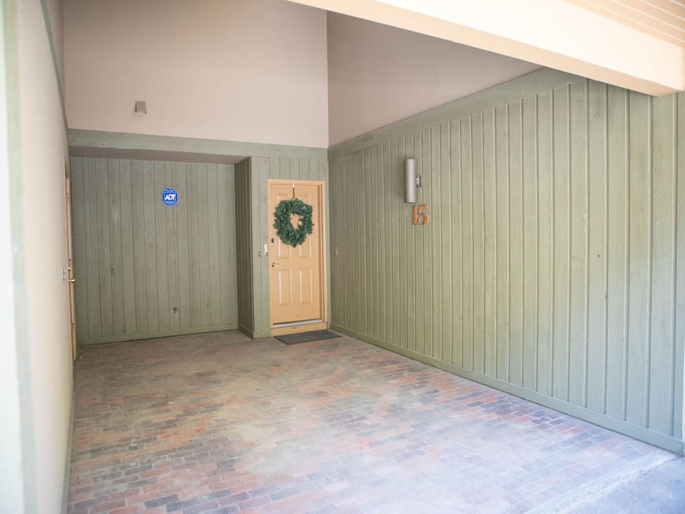 Covered entrance with yellow door, wreath, and "15" on the green wall. Brick flooring.