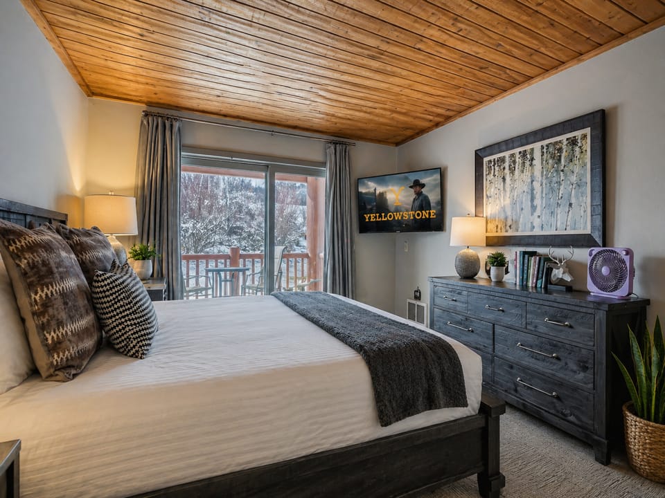Unwind in your cozy bedroom with rustic wood ceilings, a plush bed, and snowy mountain views from your private balcony—your perfect mountain escape.