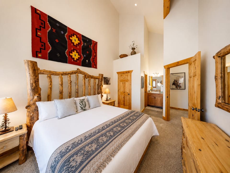 Sink into crisp white linens in your rustic mountain bedroom, where handcrafted log furniture and warm wood tones create a cozy, welcoming retreat after your day's adventures.