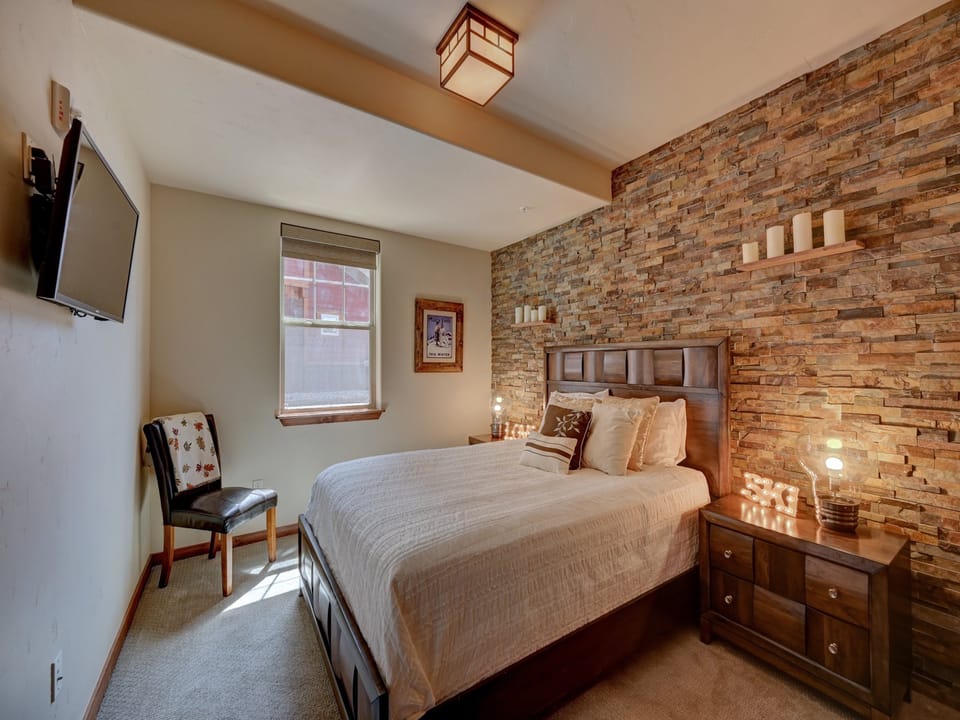 A modern decor queen size bedroom with a stone accent wall, with a window to shower the room with natural light