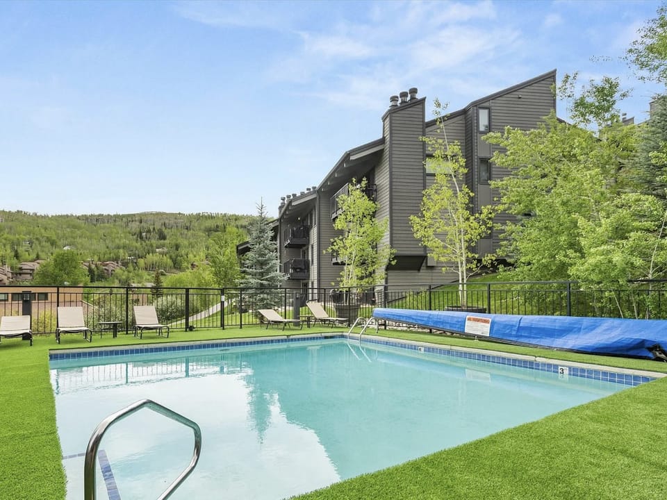 A sparkling outdoor pool surrounded by lush green lawns, lounge chairs, and mountain views, creating the perfect spot to relax under sunny skies after your adventures.