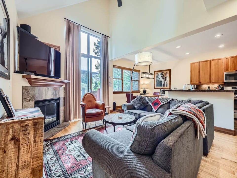 Curl up in your spacious living room where the crackling fireplace and plush gray sofa create the perfect spot for evening relaxation, while natural light streams through tall windows into your open-concept haven.
