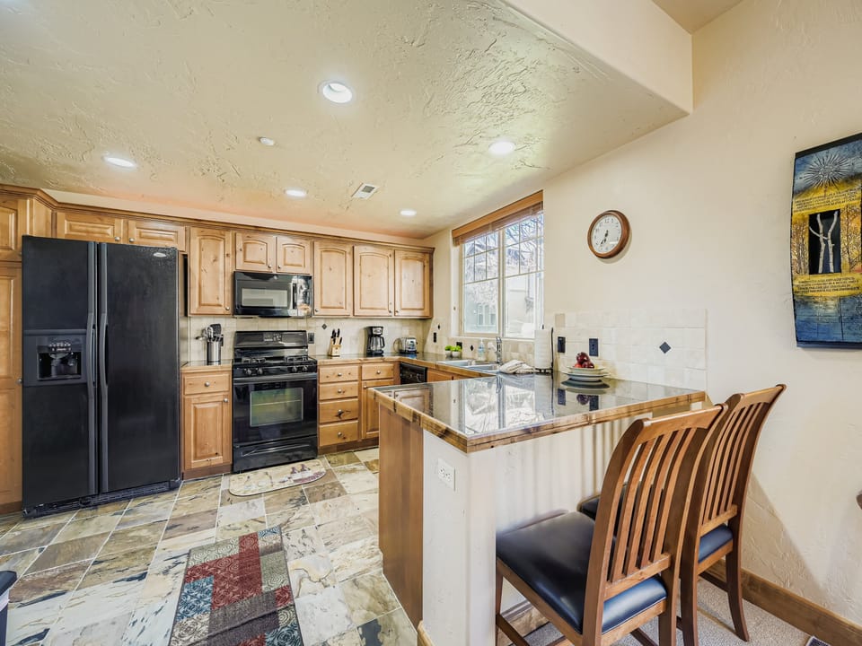 Your fully-equipped kitchen awaits with warm wood cabinetry, granite counters, modern appliances, and an inviting breakfast bar for casual meals and conversation.