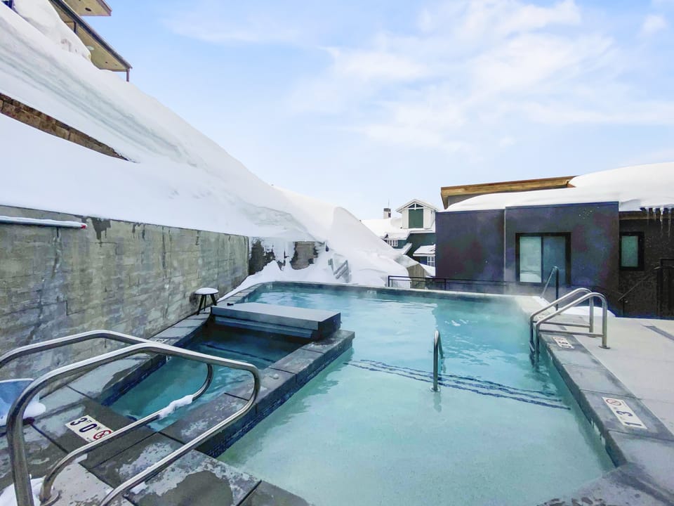 A heated outdoor pool and hot tub set against a snowy mountain backdrop, offering a serene alpine retreat for relaxation after a day on the slopes.