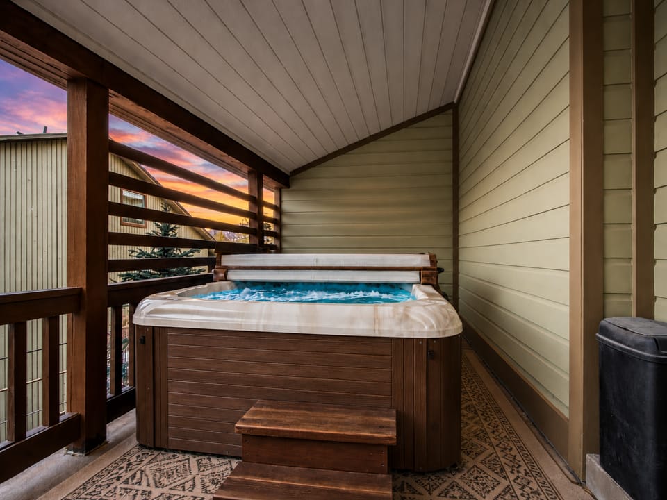 Unwind in your private hot tub on the covered balcony as the sun sets, painting the sky in soft hues just beyond the trees.