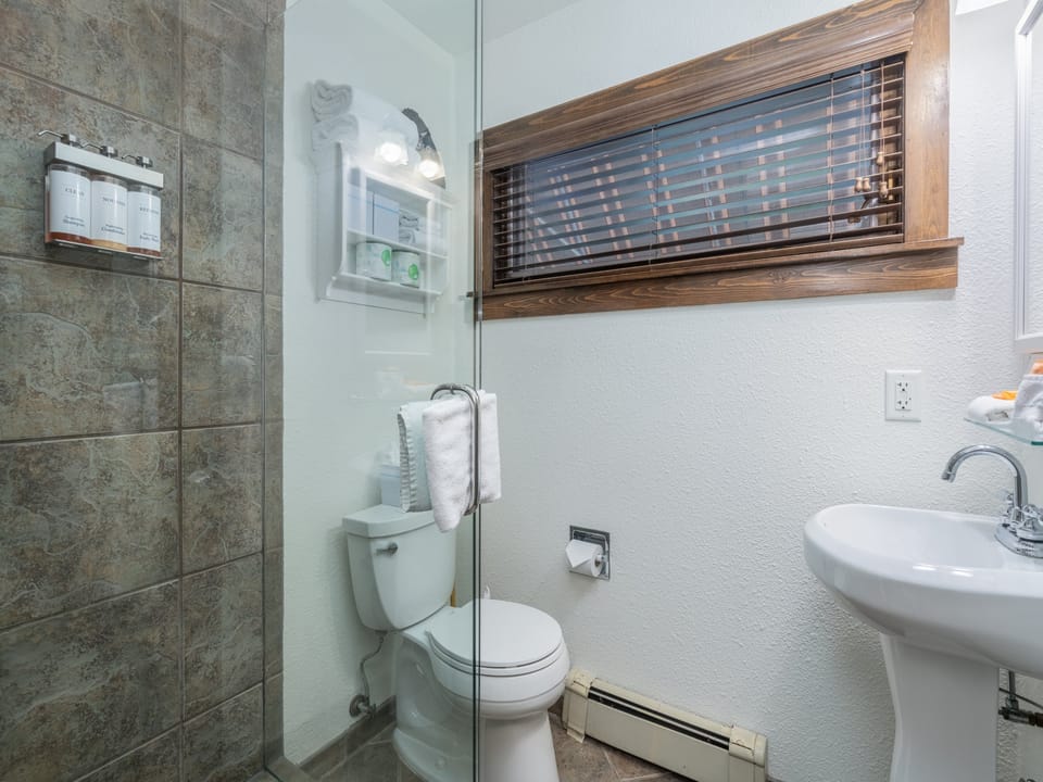 Your private bathroom features a walk-in shower with elegant stone tile, a pedestal sink, and crisp white linens—a refreshing space to start and end your day.
