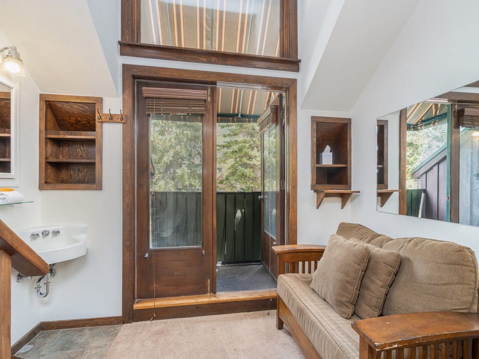A cozy living space featuring vaulted ceilings and large windows that frame natural light and greenery. Settle in on the comfortable sofa, enjoy the rustic charm of wooden accents, and step out to your own private outdoor retreat just beyond the door.
