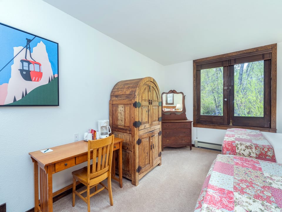Your comfortable bedroom features rustic wood furnishings, a charming mountain-view window, and a cozy work desk—perfect for unwinding after a day of mountain adventures.