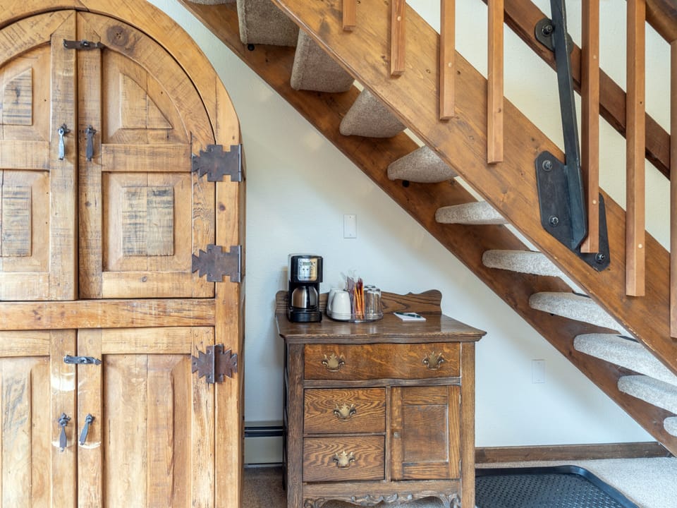 Warm wooden accents frame this inviting space where every detail invites relaxation. Your morning coffee awaits on the antique chest, and carpeted stairs lead you upward to your retreat.