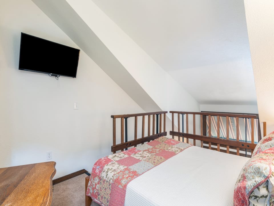 Your cozy loft bedroom awaits with vaulted ceilings, plush bedding, and a wall-mounted TV for unwinding after exploring the area.