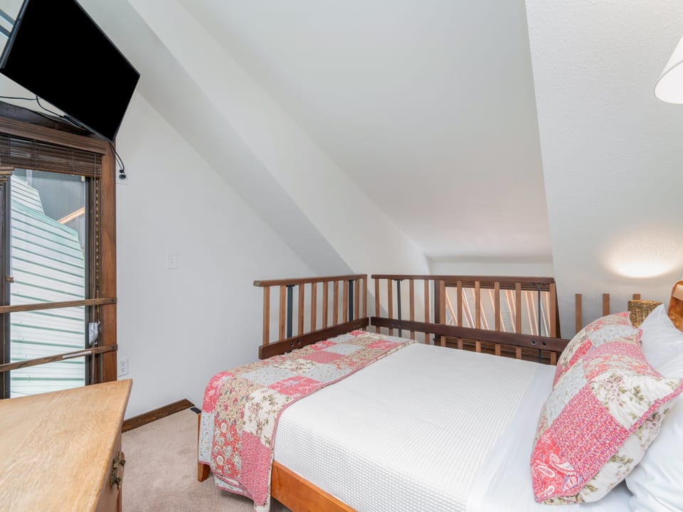 Your cozy loft bedroom features a charming wooden railing, plush bedding with warm quilted accents, and modern entertainment for peaceful rest.