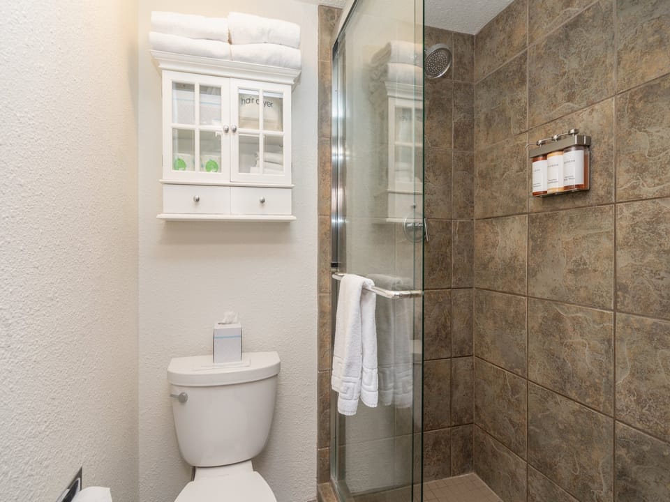 Your private bathroom features a sleek glass-enclosed shower with rustic stone tile, fluffy towels, and a charming cabinet for your essentials.