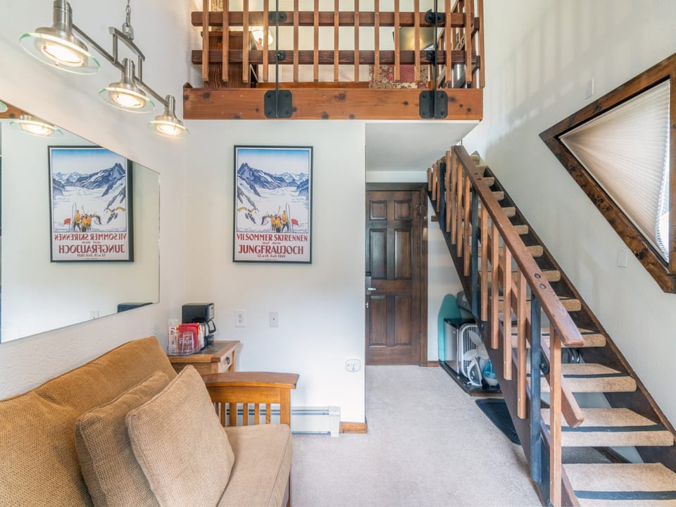 Cozy alpine-inspired loft with vintage ski posters, warm wood beams, and a clever space-saving staircase leading to your sleeping area above.
