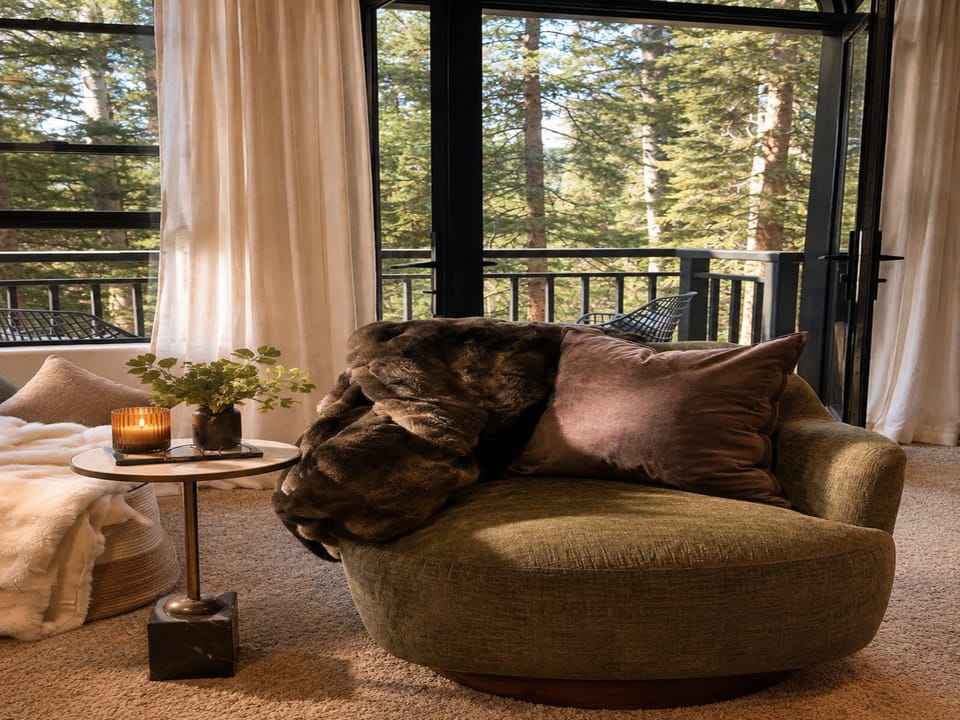 Curl up in your cozy chair with a view of towering pines through floor-to-ceiling windows. Soft throws and warm candlelight create the perfect mountain retreat.