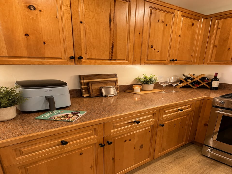 Your fully equipped kitchen invites you to cook at home with warm wood cabinetry, ample counter space, and thoughtful touches like a wine rack and fresh greenery to make every meal feel special.