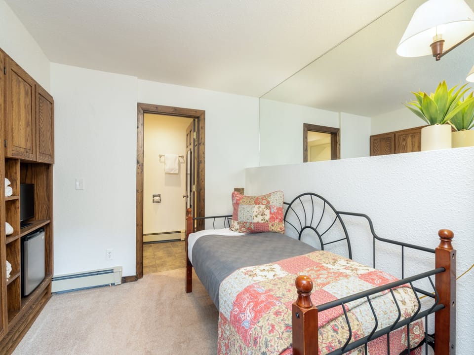 Your cozy sleeping space features a charming metal bed dressed in colorful quilted bedding, with a convenient en-suite bathroom just steps away for your comfort.