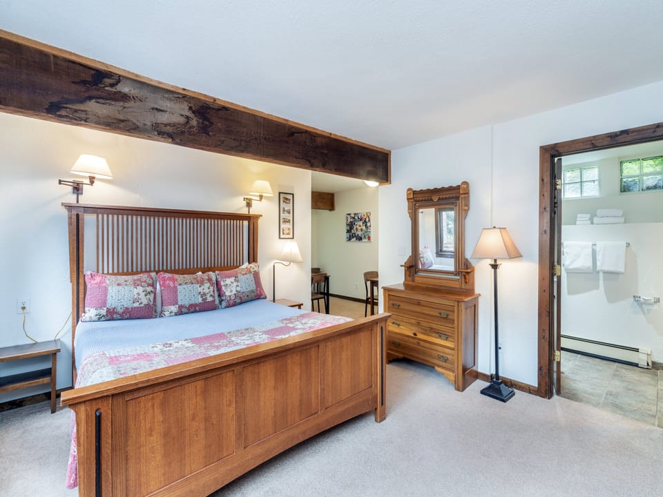 Unwind in this charming bedroom featuring rustic wooden beams, a cozy handcrafted bed, and warm lighting that creates a peaceful retreat after your day exploring.