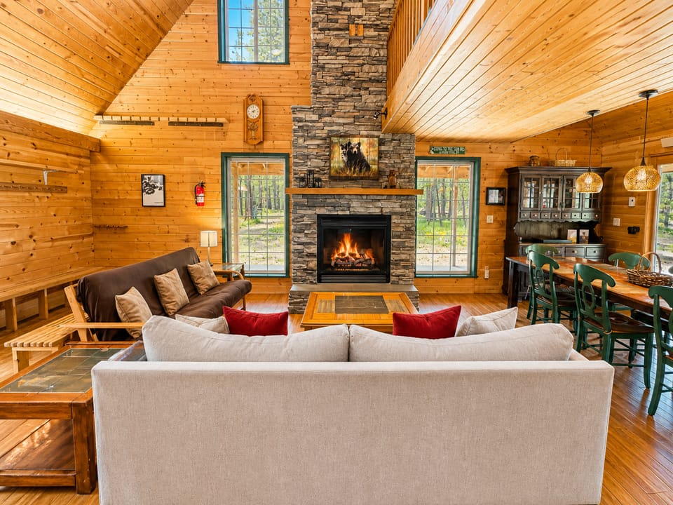 Gather around the glowing stone fireplace in this warm, wood-paneled living space. Vaulted ceilings and forest views create your perfect mountain retreat, blending rustic charm with cozy comfort for relaxing evenings together.