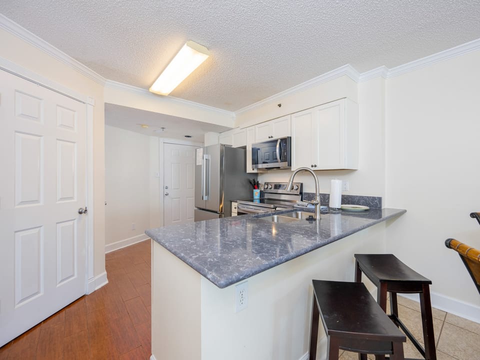 This kitchen features white cabinetry, essential appliances, and a breakfast bar with seating, perfect for casual dining