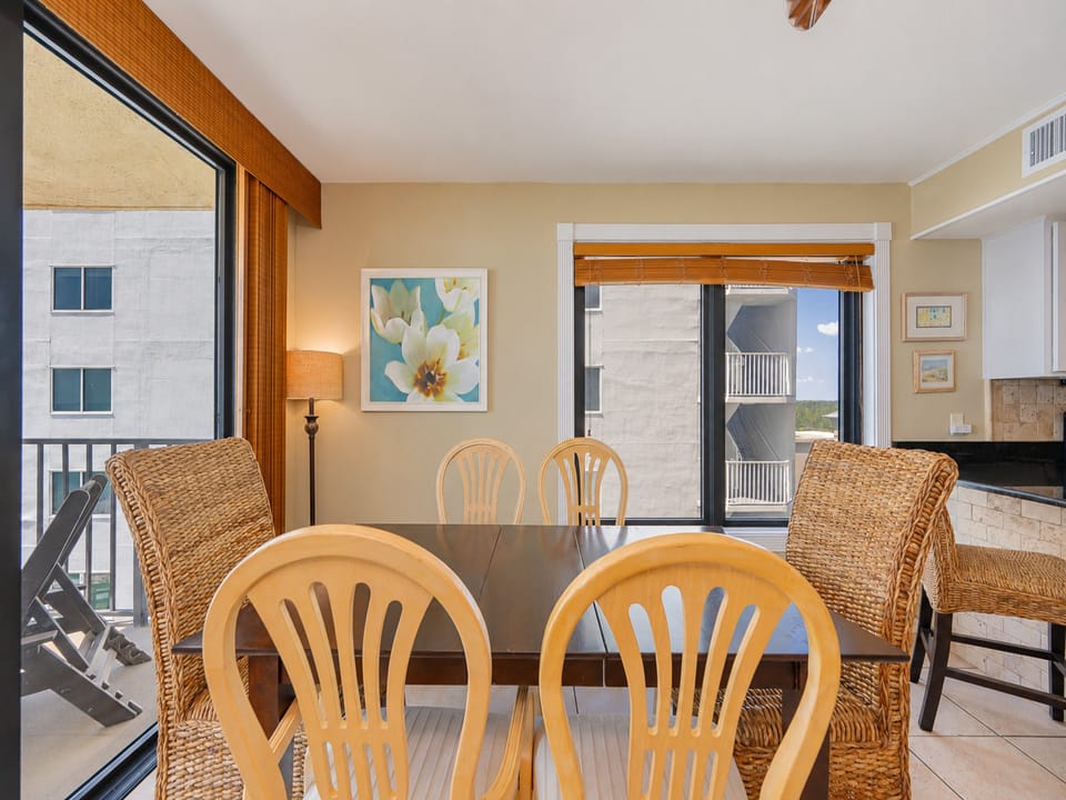 The living area features a glass breakfast table with woven chairs, a couch with queen sleeper, TV, and beautiful beach view