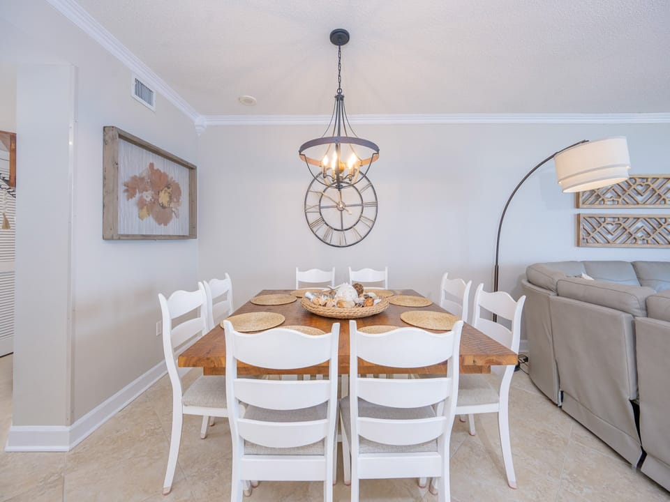 Stylish dining area features a rustic wooden table with white chairs, complemented by a cozy living space and balcony views
